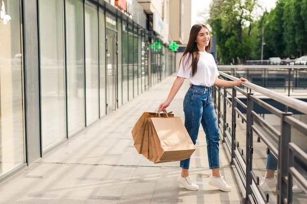 Mujer joven feliz con bolsas de compras caminando por la calle de la tienda.