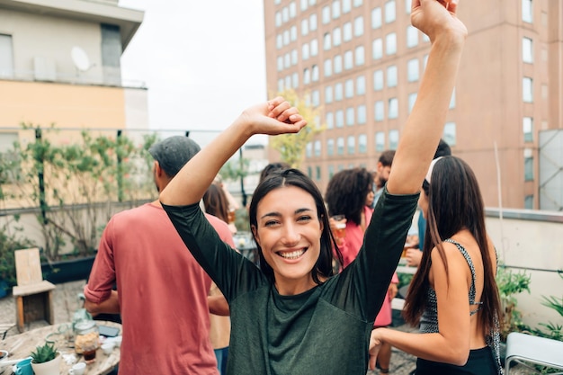 Mujer joven feliz con los brazos levantados mientras baila en la fiesta de estudiantes universitarios