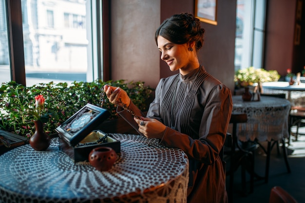 Mujer joven feliz en café con ataúd y joyas