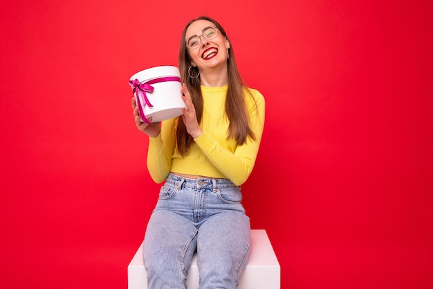 Mujer joven feliz con una caja de regalo blanca sobre un fondo rojo.