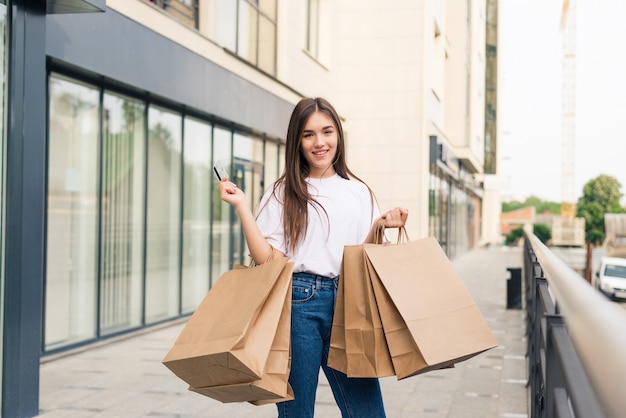 Mujer joven feliz caminando con bolsas de la compra al aire libre en la calle