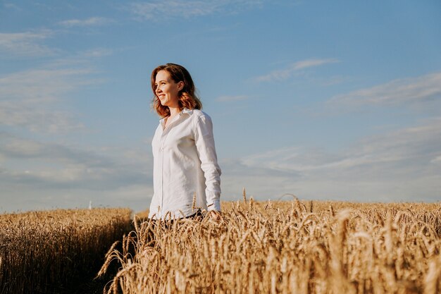 Mujer joven feliz con una camisa blanca en un campo de trigo. Día soleado. Chica sonriendo, concepto de felicidad