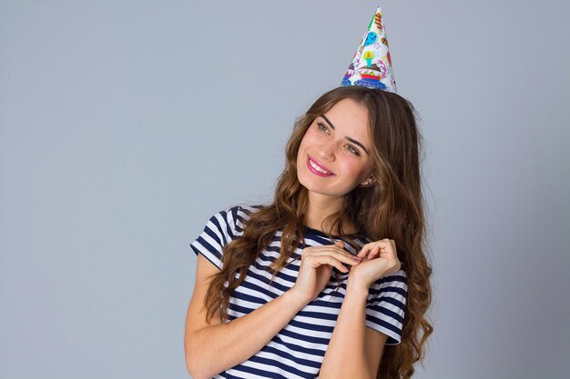 Mujer joven feliz con camiseta despojada y gorra de celebración con fondo gris en el estudio