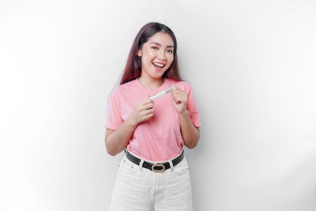 Mujer joven feliz con camiseta rosa que muestra su prueba de embarazo y una imagen de ultrasonido aislada en el concepto de embarazo de fondo blanco