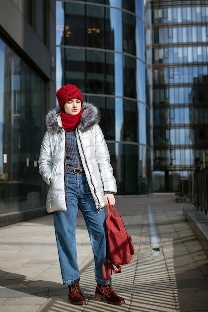 Mujer joven feliz con una chaqueta y un sombrero rojo, con una mochila viaja por las ciudades