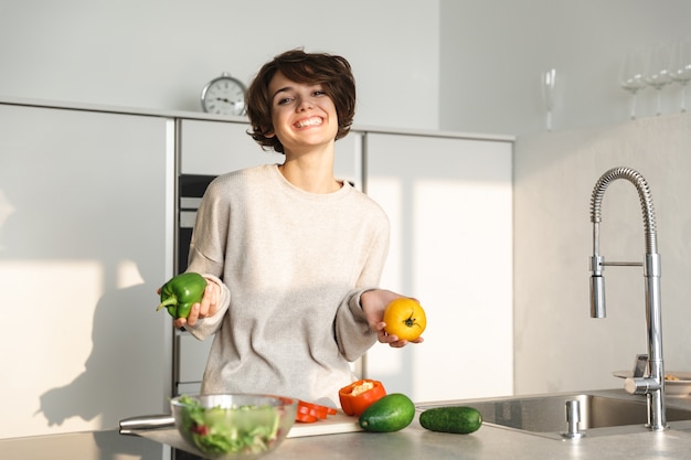 Mujer joven feliz cocinar ensalada fresca en la cocina de casa