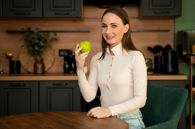 Foto mujer joven feliz está comiendo una manzana en la cocina dieta el concepto de una dieta alimentos saludables