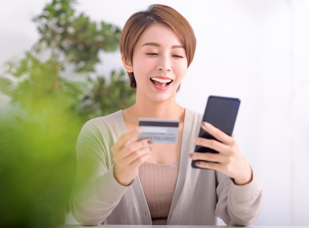 Mujer joven feliz comprando en línea con teléfono móvil y tarjeta de crédito