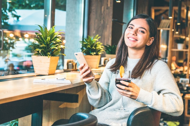 Mujer joven feliz con copa de vino revisando el teléfono