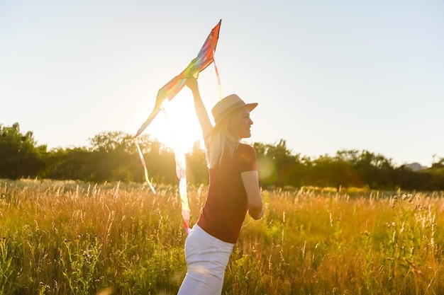 Mujer joven feliz corriendo con una cometa en un claro al atardecer en verano