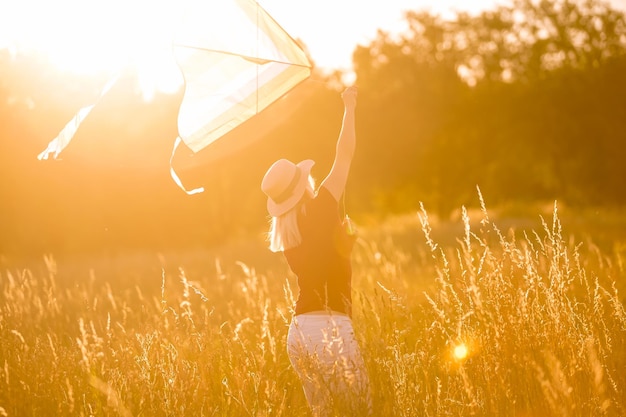 Mujer joven feliz corriendo con una cometa en un claro al atardecer en verano