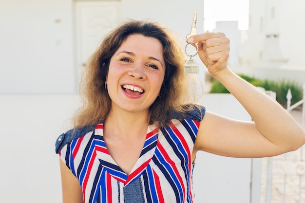 Mujer joven feliz delante de la casa nueva con las llaves de la casa nueva cerrar