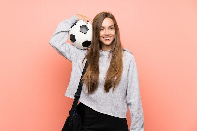 Mujer joven feliz del deporte sobre la pared rosada aislada que sostiene un balón de fútbol