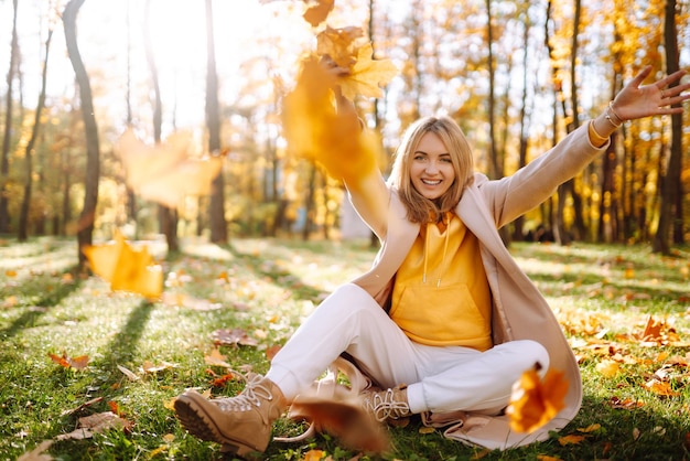 Mujer joven feliz divirtiéndose con hojas en el parque de otoño