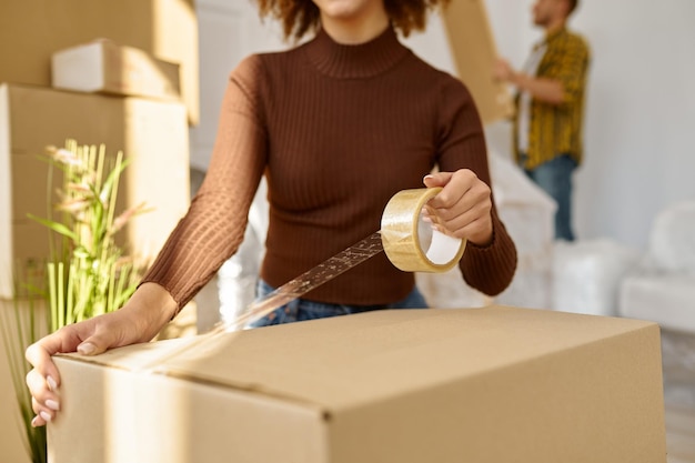 Mujer joven feliz empacando una caja de cartón para mudarse a un nuevo apartamento de pie en la sala de estar