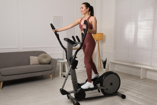 Mujer joven feliz entrenando en máquina elíptica en casa