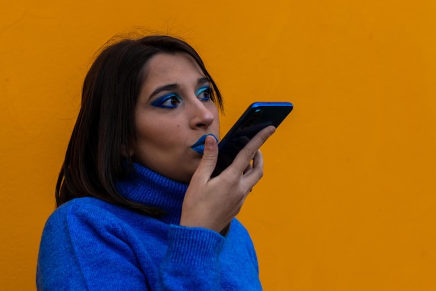 Mujer joven feliz enviando un audio de voz con su teléfono celular en un fondo naranja