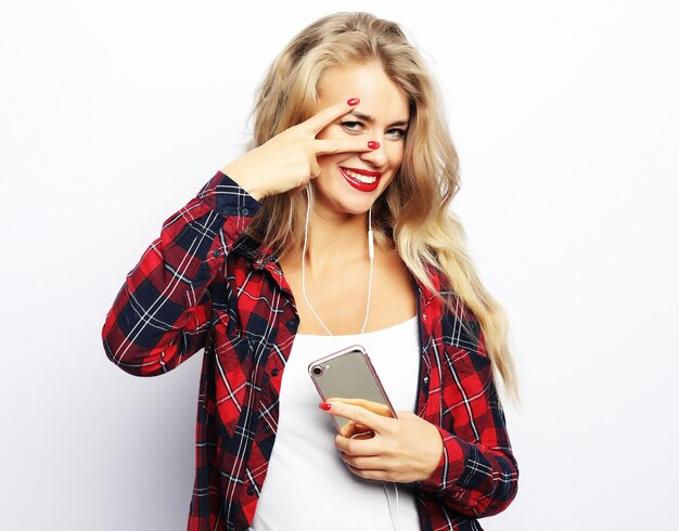 Mujer joven feliz escuchando música desde un teléfono inteligente sobre blanco
