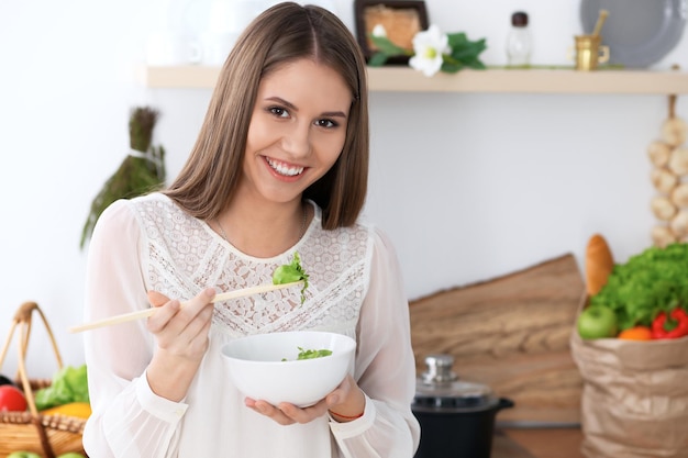 Mujer joven feliz está cocinando o comiendo ensalada fresca en la cocina. Concepto de alimentación y salud.