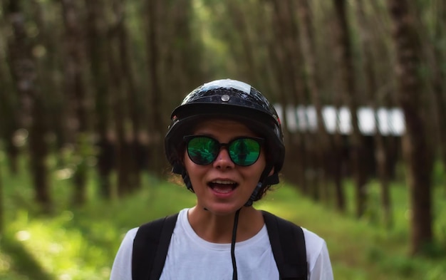 Mujer joven feliz en gafas de sol y casco contra los árboles Vacaciones