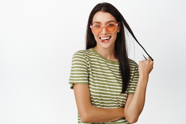 Mujer joven feliz con gafas de sol sonriendo y luciendo alegre yendo de vacaciones de verano de pie sobre fondo blanco