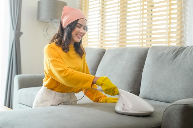 Mujer joven feliz con guantes amarillos y aspiradora Limpiando un sofá en la sala de estar