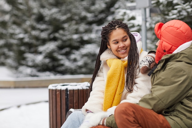 Mujer joven feliz hablando con su novio mientras están sentados en un banco en el parque