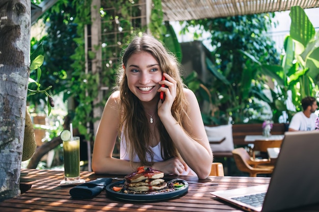 Mujer joven feliz hablando por teléfono durante el desayuno