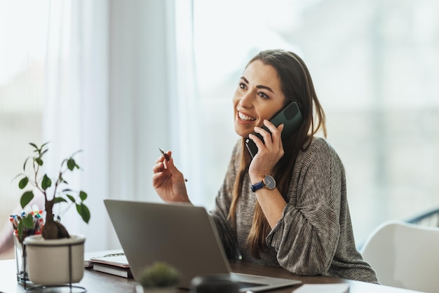 Mujer joven feliz haciendo trabajo independiente durante una llamada.