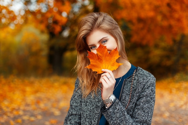 Mujer joven feliz con una hermosa hoja amarilla coloreada disfrutando del día de otoño