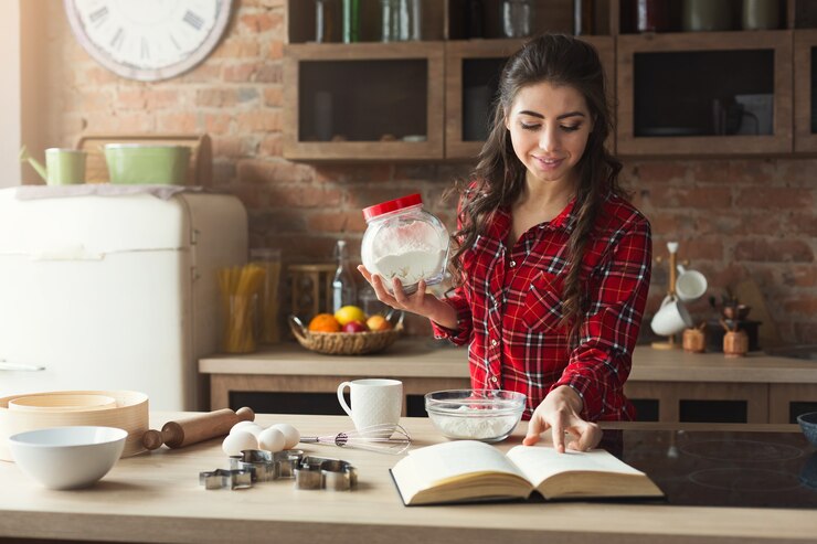 Foto mujer joven feliz horneando pastel en la cocina del desván en casa, usando el libro con la receta. maqueta, espacio de copia