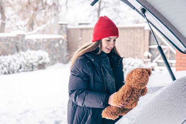Mujer joven feliz en invierno encontró un oso de peluche en el maletero de un coche