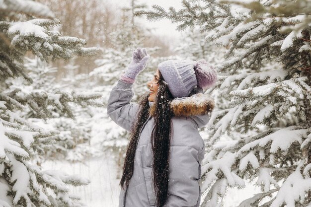 Mujer joven feliz en invierno en un paseo por la naturaleza. una mujer con una chaqueta lila se encuentra cerca de los árboles de Navidad en un parque de invierno.