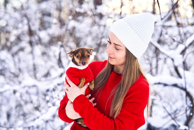 Mujer joven feliz en invierno, sostiene en sus brazos y juega en la nieve con su perro, mascota chihuahua.