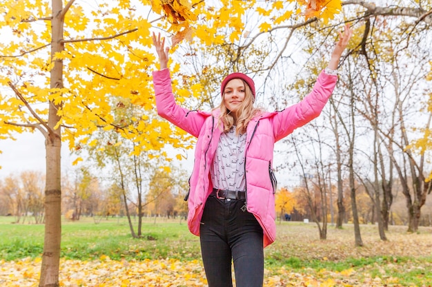 Mujer joven feliz jugando bajo las hojas amarillas que caen en el hermoso parque de otoño en la naturaleza camina al aire libre. Adolescente vomita hojas de arce naranja otoñal.