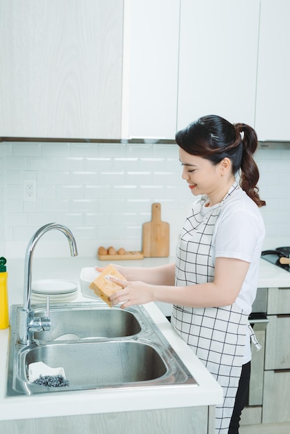 Mujer joven feliz lavando platos en la cocina