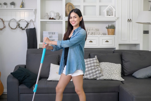 Mujer joven feliz limpiando el piso con un trapeador en el salón