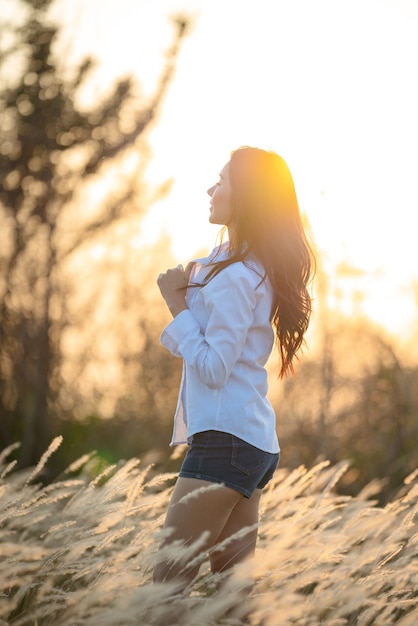 Mujer joven feliz en lindo vestido de verano de pie en el campo a la luz del atardecer