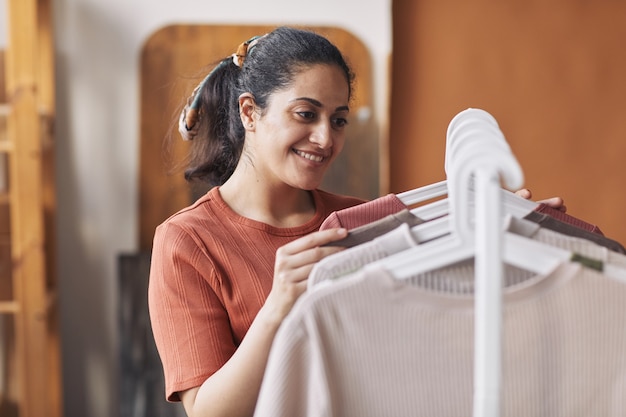 Mujer joven feliz mirando nuevas camisetas en el estante y eligiendo la nueva para ella