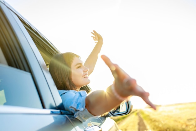 Mujer joven feliz mirando por la ventana del coche al atardecer dorado en el campo