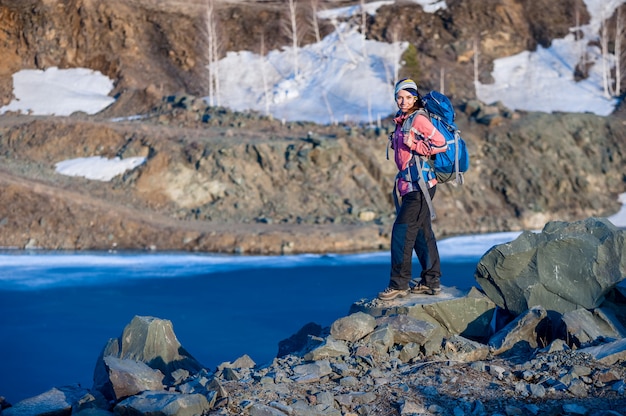 La mujer joven feliz con una mochila sonríe en el lago