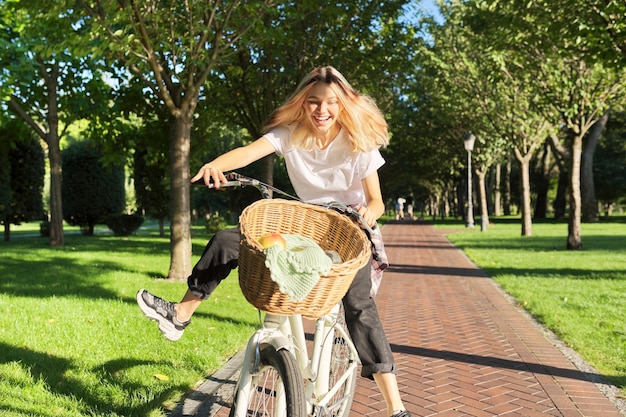 Mujer joven feliz montando en bicicleta en la carretera en el parque hermosa adolescente hipter divirtiéndose y riendo