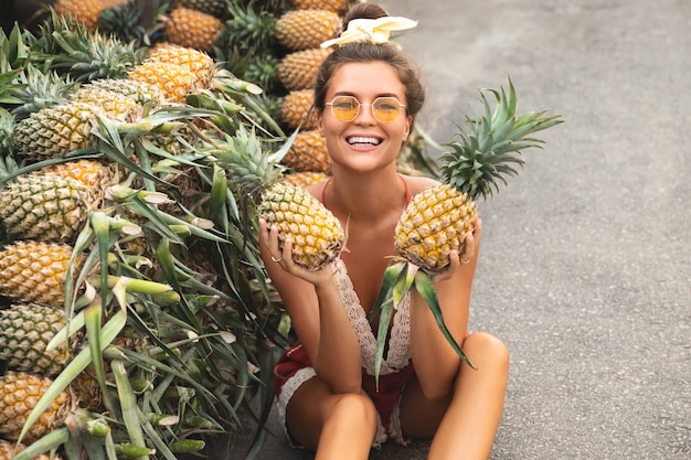 Mujer joven y feliz con un montón de piñas en el mercado