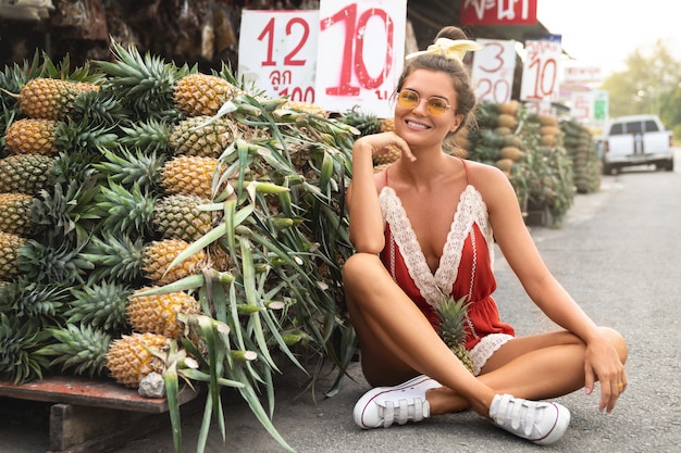 Mujer joven y feliz con un montón de piñas en el mercado