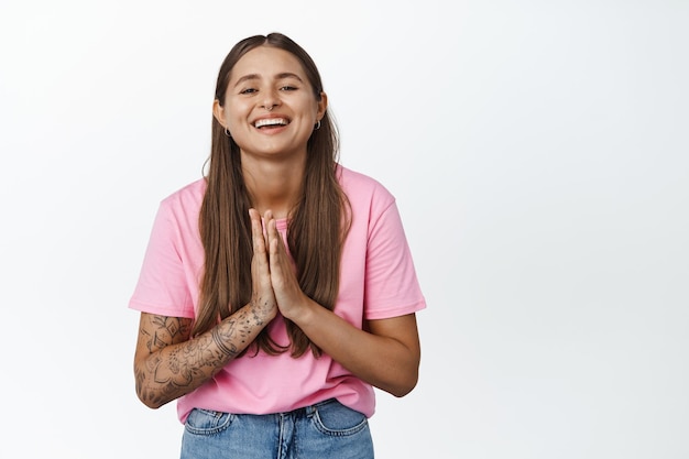 Mujer joven feliz mostrando oración, gesto namaste y sonriendo, mostrando gesto de agradecimiento, rogando por algo o agradecida, de pie sobre fondo blanco.