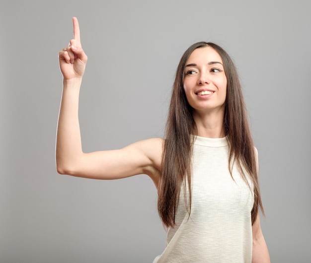 Mujer joven feliz mostrando con su dedo índice aislado sobre fondo gris