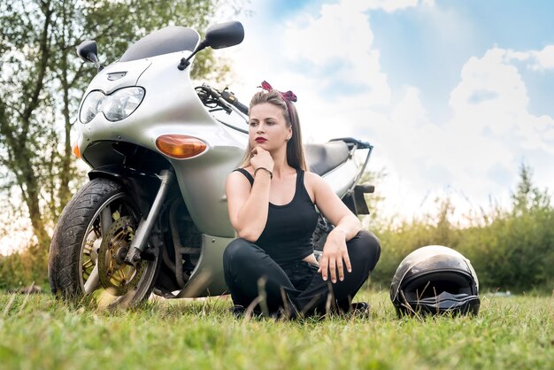 Mujer joven y feliz en moto posando al aire libre