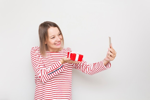 Foto mujer joven feliz muestra una caja de regalo cuando habla por teléfono.