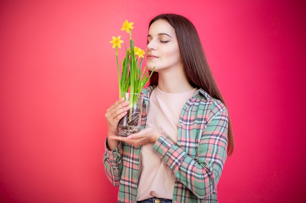 Mujer joven feliz oliendo la planta de narciso sobre fondo rosa