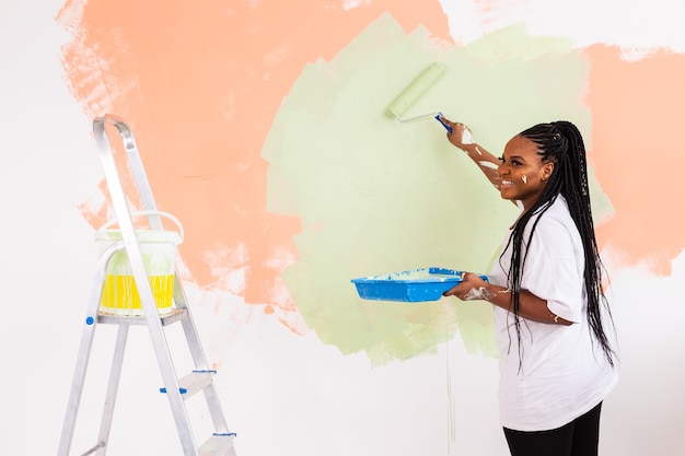 Mujer joven feliz pintar la pared interior con rodillo de pintura en casa nueva
